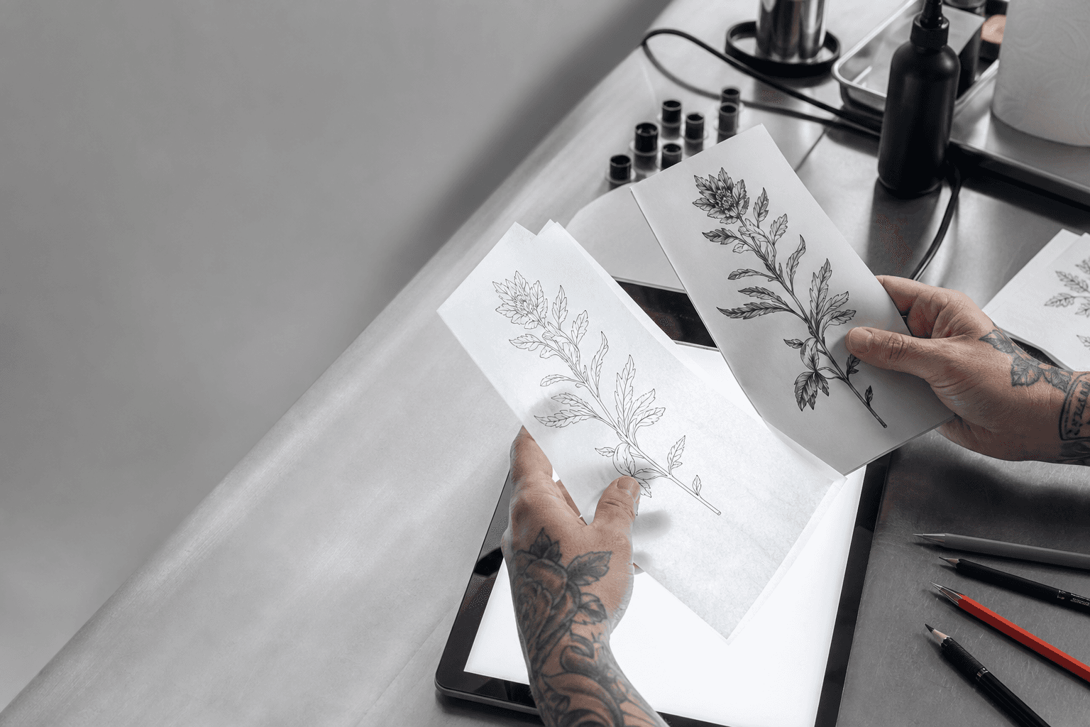 Tattoo artist preparing botanical artwork and stencil linework at a studio station